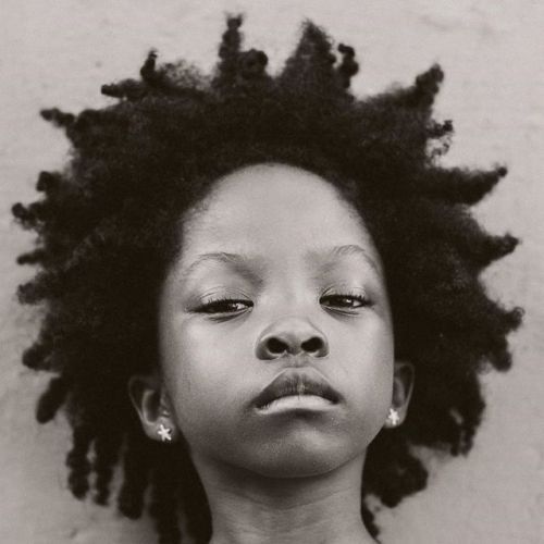 a young black girl with a serious expression stares straight ahead. she has an afro hairstyle.  the image is a close up of her face.