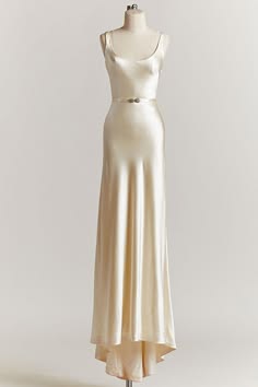 a white satin dress with a simple, sleeveless design and a floorlength skirt. the dress is displayed on a mannequin against a white background. it has a thin silver belt at the waist.