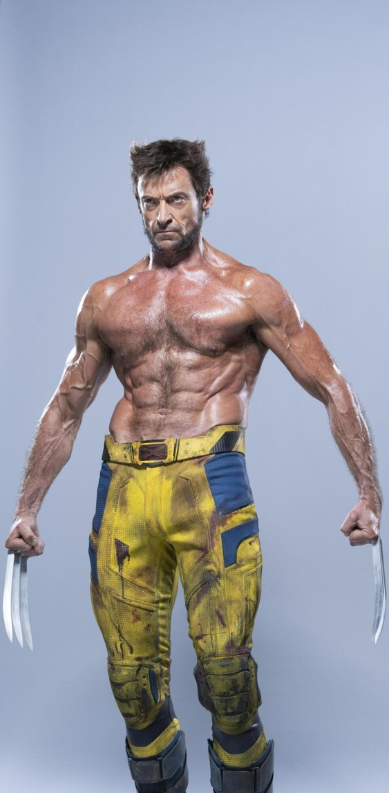 a fullbody portrait of hugh jackman as wolverine from the xmen/marvel comics franchise. he is shown barechested, with prominent musculature and his signature claws extended. he is wearing a yellow and blue superhero costume. the background is a neutral grey.