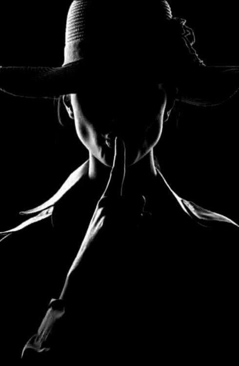 a black and white silhouette of a woman in a hat, her finger is placed over her lips as if to silence a