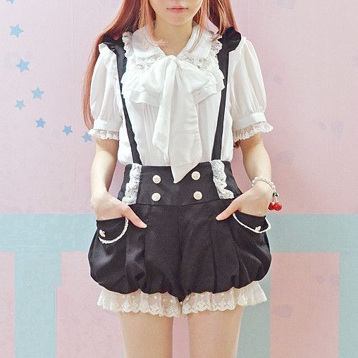 a young woman is posing in a pastel pink room. she is wearing a lolita fashion outfit, which consists of a white blouse with a large collar, black bloomers with lace trim, and black suspenders. she is also wearing a pink hair bow and has her hair styled in long, loose curls.  the lighting is bright and artificial, and the perspective is at eye level.