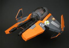 this is a photo of a lego star wars toy, namely, a starfighter with a transparent cockpit, two frontfacing laser cannons, and a droid clinging to the side.