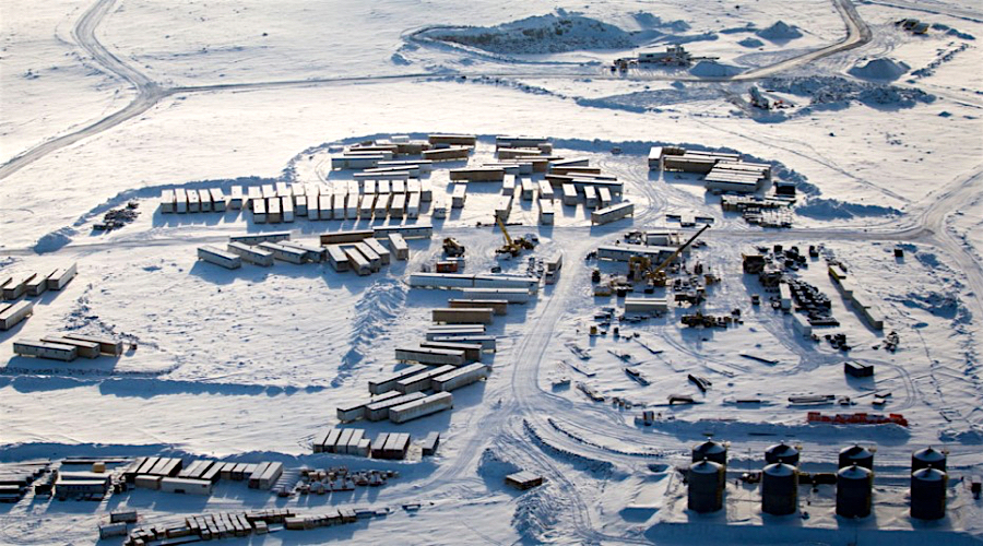an aerial view of a snowcovered construction site in a remote, arctic location. the site is covered in snow and ice, with numerous buildings and industrial equipment scattered around. the site appears to be an oil rig or drilling platform, with a network of pipes and storage tanks visible. the surrounding landscape is flat and tundralike, with no trees or other vegetation. the image captures the harsh beauty of the arctic environment and the human impact on it.