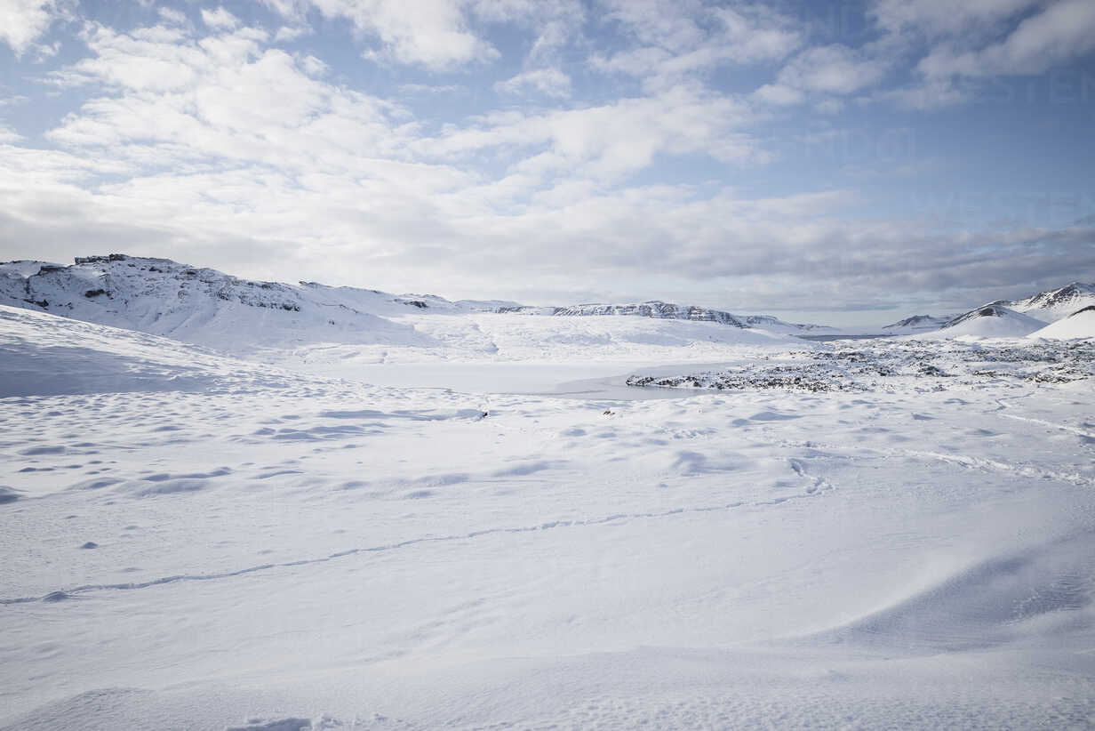 a panoramic view of a snowcovered landscape with mountains in the distance. the sky is a clear blue with fluffy white clouds. the snow is pristine and white, and the scene is very serene.