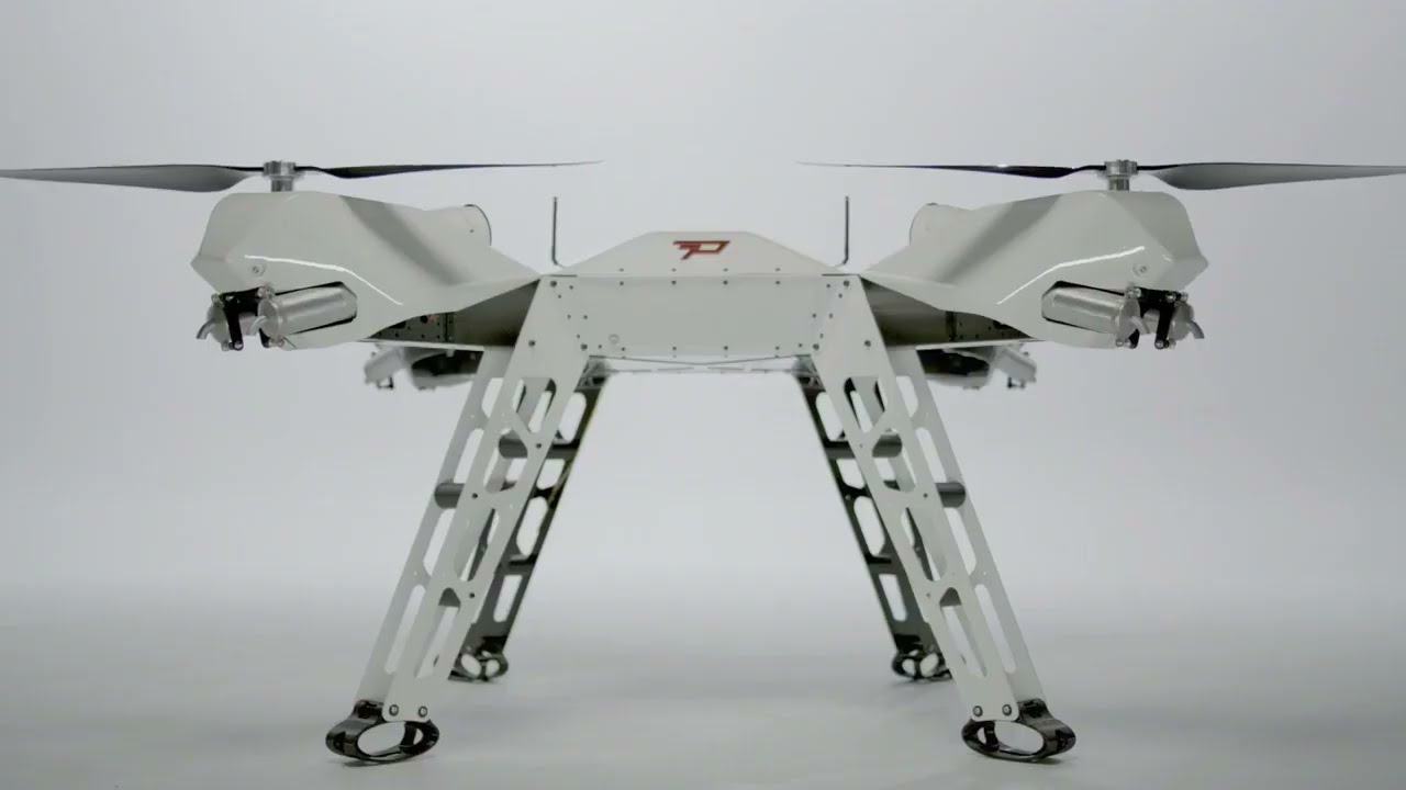 a white drone with a metal frame and landing gear, with four propellers. the drone is in a white studio setting and is facing the camera.