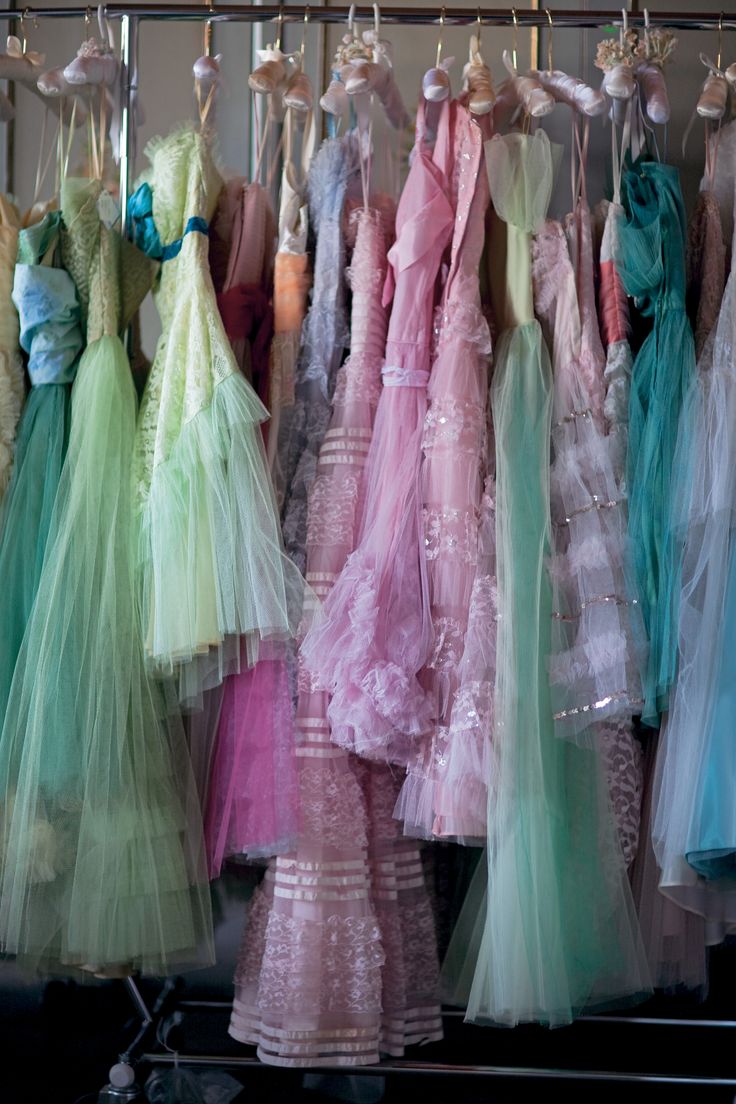 a rack of beautiful tulle dresses in a variety of pastel colors. the dresses are all very feminine and delicate, with frills and lace. they look like they would be perfect for a special occasion. the dresses are hanging on a rack in a store or boutique.