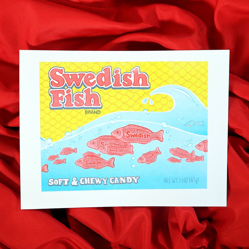 the image shows a highquality print or artwork that mimics the vintage packaging of swedish fish candy.  the print features a bright yellow background with a light blue wave depicting several red swedish fish candies swimming.  the text "swedish fish" is prominently displayed in a retro font, along with the description "soft & chewy candy".  the overall style is reminiscent of classic candy packaging from the late 20th century. the print is displayed on a red fabric background.