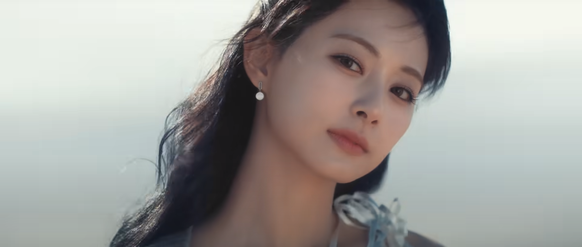 a closeup portrait of a young asian woman with dark hair and delicate features. she's wearing a lightcolored dress and holding a violin, possibly posing for a music video or photoshoot. the background is a blurry beach scene bathed in soft, natural light, creating a serene and ethereal atmosphere.