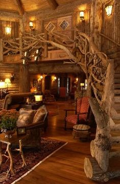 the image shows the interior of a rustic log cabin. the focal point is a staircase built around a tree trunk, with wooden branches forming part of the railing. the living room area features a sofa, an armchair, a table with flowers, and a patterned area rug. the furniture and decor have a warm, earthy tone, complementing the log walls and wooden floors. lighting fixtures are placed throughout the space, enhancing the cozy and inviting atmosphere. there is also an ottoman near the armchair.