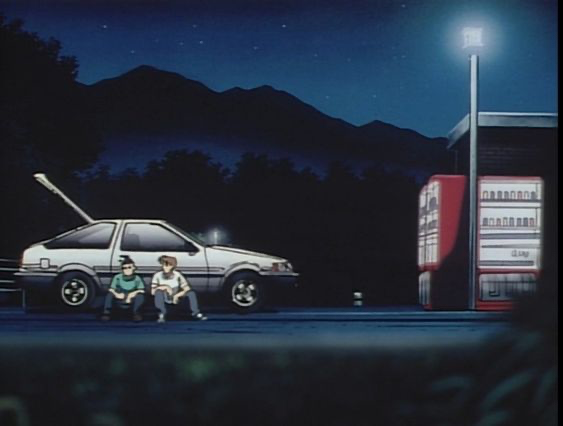 two young men are sitting in front of a white hatchback at night. they appear to be at a deserted rest stop with a vending machine and a street lamp. mountains are in the background, silhouetted against the dark blue night sky. the overall mood is peaceful and contemplative.