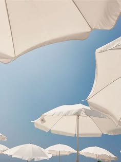 a photo of a group of white umbrellas arranged in a row, against a clear blue sky. the umbrellas are open and providing shade from the sun.