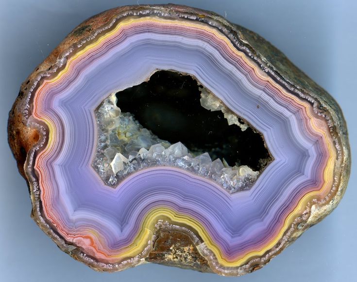 a closeup of a cut and polished agate geode, showcasing layers of purple, yellow, orange, and brown banding around a central cavity lined with small crystals.