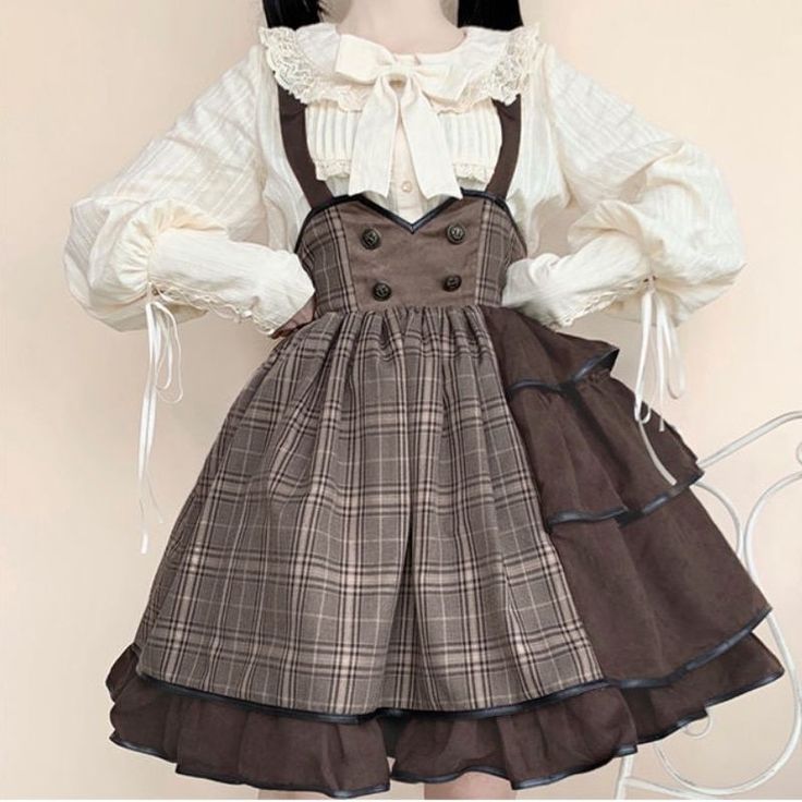 a woman is wearing a brown and white lolita fashion dress. the dress has a plaid pattern and is layered with ruffles. she is also wearing a white blouse with a peter pan collar and a brown bow. the photo is taken indoors in bright, natural light.