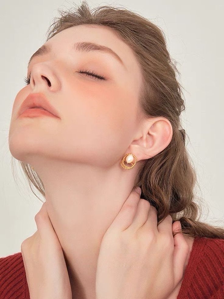 loseup portrait of a young woman with long brown hair, wearing gold pearl earrings. she's wearing a red sweater and has a soft, natural makeup look.  the focus is on her face and the earrings, highlighting her beauty and the delicate jewelry.  the background is a simple, lightcolored backdrop.