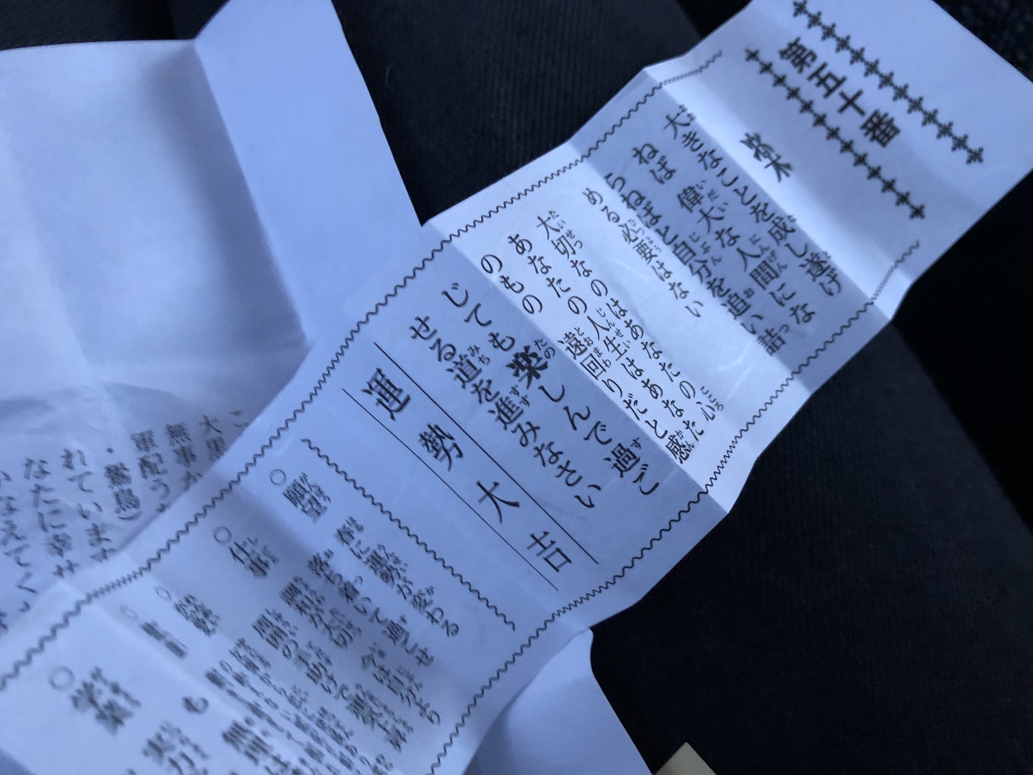 the image shows two japanese fortune slips, known as omikuji, laying on top of one another. the text is written in black ink on white paper and contains predictions and advice.  the visible portion of the top slip reveals it to be a "daikichi" (大吉), meaning "great luck."