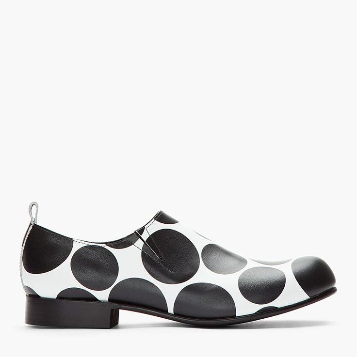 the image shows a single women's slipon shoe.  the shoe is made of leather and features a bold black and white polka dot pattern.  the style is a simple, roundedtoe flat, with a minimalist design. the shoe has a slight pull tab at the back. the overall aesthetic is modern and fashionable.