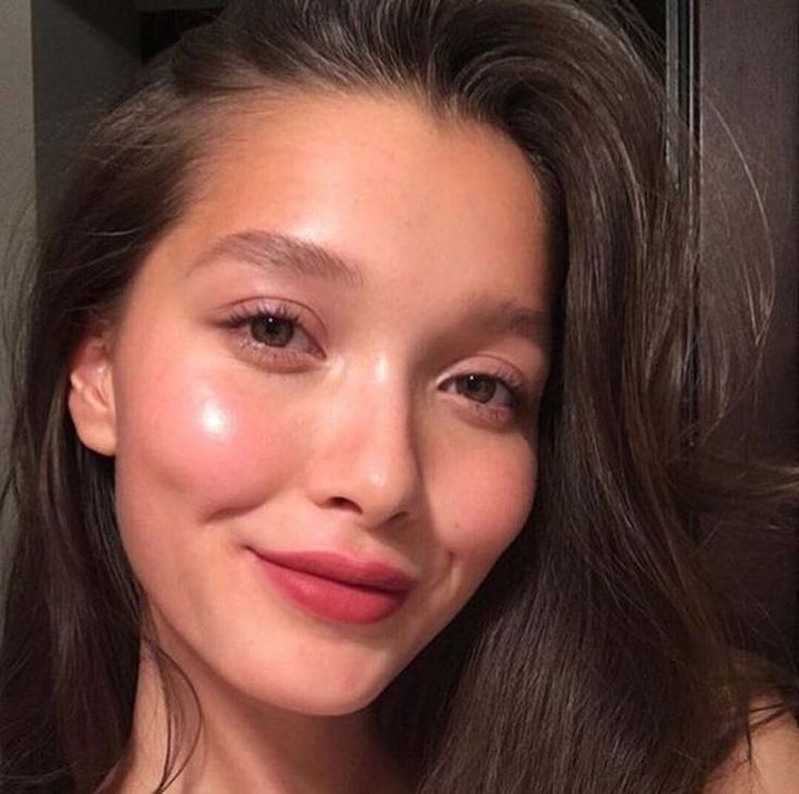 a portrait of a woman with brown hair and brown eyes, smiling at the camera. her skin is glowing, and she is wearing lipstick and makeup. it looks like a selfie.