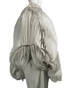 a white dress with pleated fabric throughout the entire garment. the dress is pleated into large wavy folds, creating a very dramatic look. the dress is on a mannequin without a head. the background is a simple white.