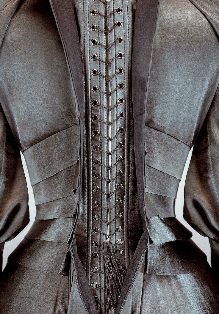 closeup shot of the back of a black satin corset with laceup detailing. the corset has a traditional design with rows of eyelets laced together with black ribbon. the fabric is layered and fitted, accentuating the waist. the overall aesthetic is reminiscent of victorian or steampunk fashion.