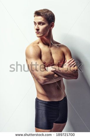 a shirtless man with a muscular physique poses with his arms crossed in front of a white background. he is wearing black shorts and has a confident expression on his face. he is looking to the side, and his muscles are clearly defined. the image is welllit and in focus.