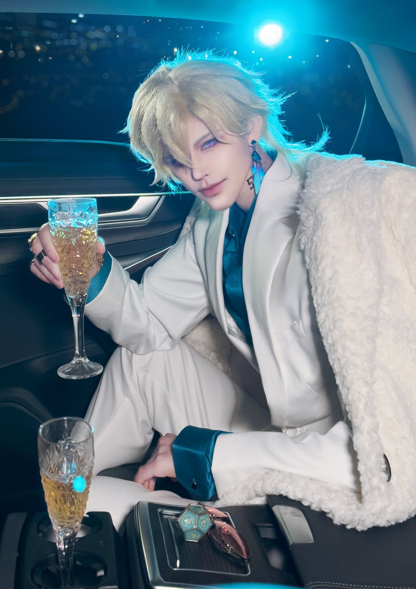 a man in a white suit, with blonde hair and blue eyes, sits in a car, looking confident and elegant as he raises a glass of champagne.
