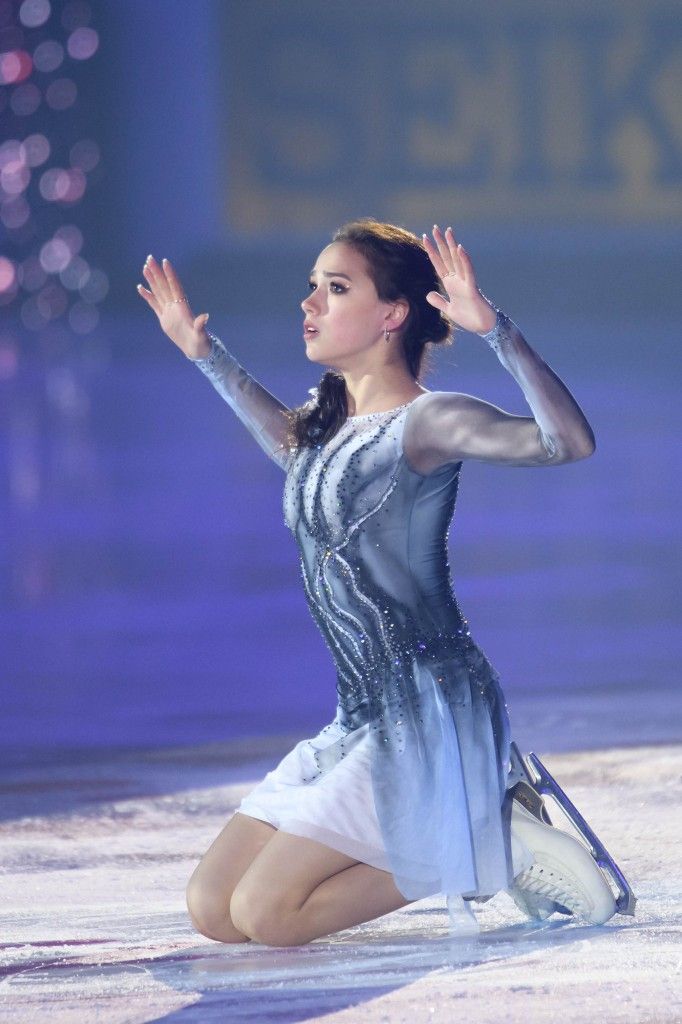 a female figure skater performs a graceful move on the ice rink during a competition. she is dressed in a beautiful white and silver skating dress. her arms are outstretched as she moves with elegance and athleticism.  she is focused on her performance, her expression is intense and determined. she is a talented athlete and a joy to watch.