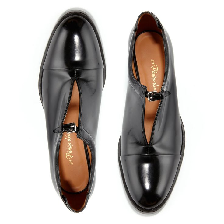 a topdown studio shot of a pair of black leather philip klein women's tstrap oxford flats.  the shoes are sleek and elegant, with a pointed toe and a cap toe detail. the shoes are positioned against a clean white background, highlighting their details.  the philip klein branding is visible inside the shoes.