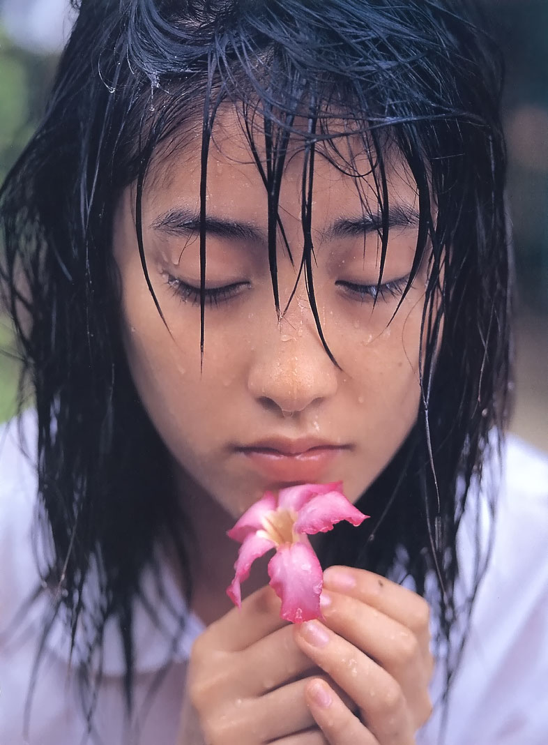 a young woman with dark, wet hair holds a delicate pink flower.  her eyes are downcast, creating a serene and contemplative atmosphere.  the soft, natural light emphasizes the water droplets clinging to her hair and the flower's petals.  the closeup perspective draws the viewer into the intimate moment.
