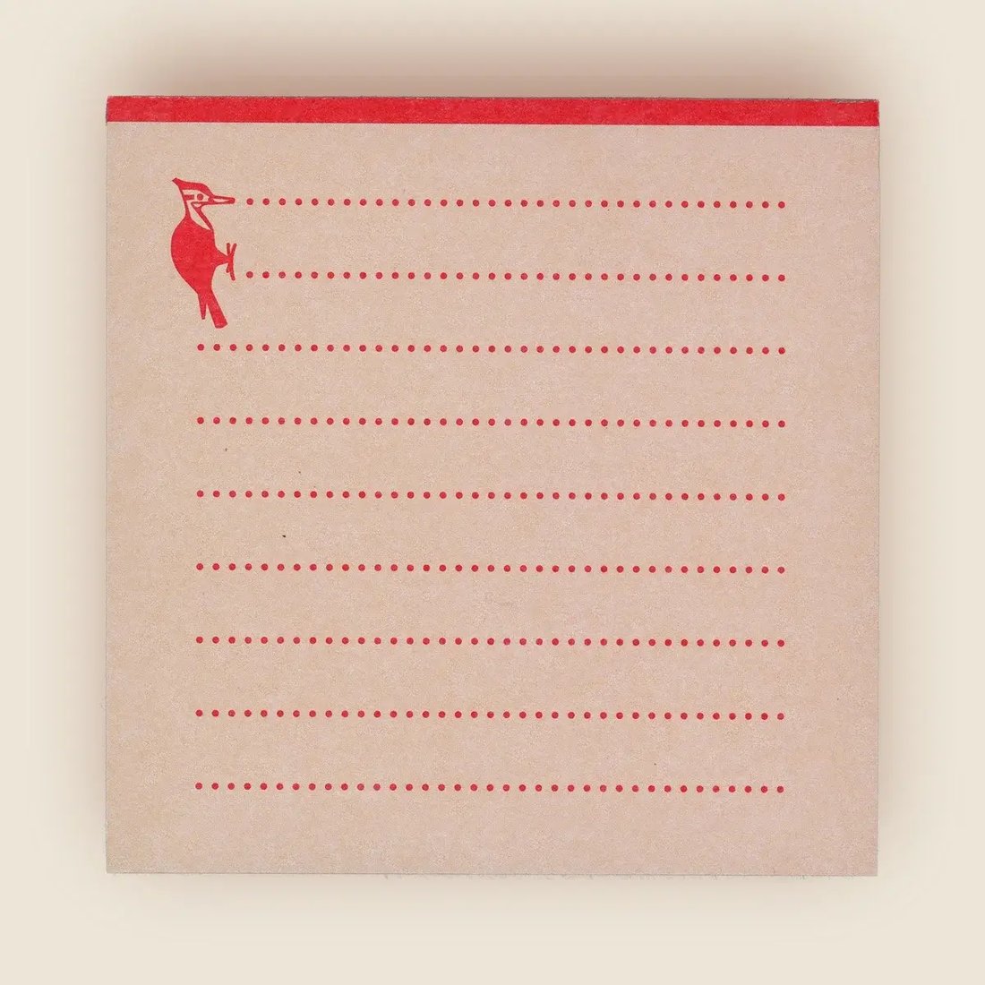 the image shows a square notepad with a light brown, textured paper.  the top edge is a contrasting red band.  red dotted lines create writing guides across the paper. a small, simple red illustration of a woodpecker is situated near the top left corner. the overall style is minimalist and slightly vintage.