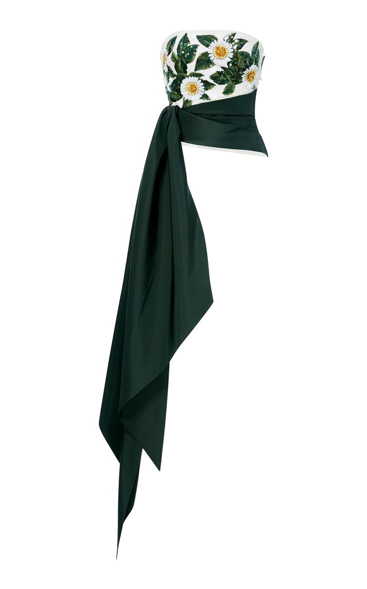 the image showcases a women's strapless top featuring a white bodice adorned with embroidered daisies and green leaves. a long, dark green sash is asymmetrically draped around the waist and extends downwards. the top appears to be made of a luxurious, structured fabric. the style is elegant and sophisticated, suitable for formal occasions.