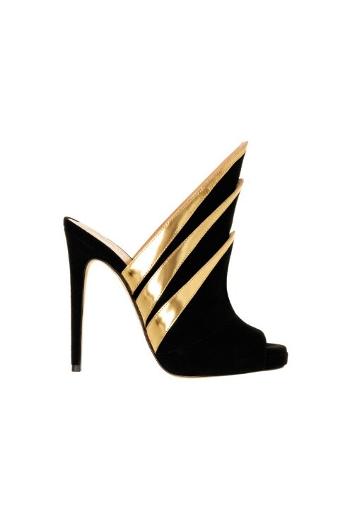 a closeup shot showcases a highheeled shoe with an open toe, featuring a sleek black suede material complemented by shiny gold accents. the design includes angular, elongated shapes extending upwards from the shoe, adding a dramatic flair. the shoe's sole is partially visible, and it is set against a plain white background.