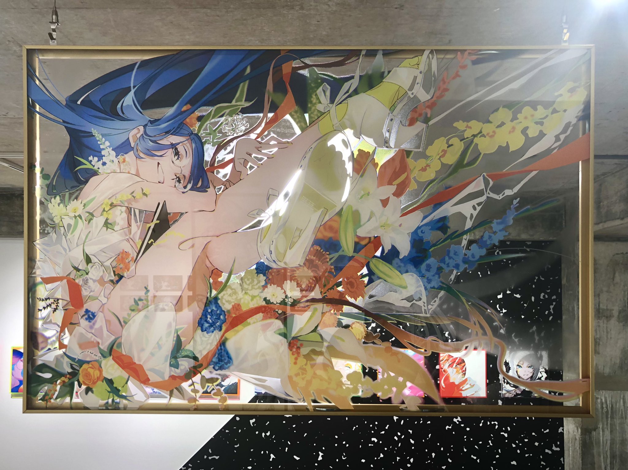 the image shows a large, framed artwork of an anime girl with blue hair. she is depicted in a dynamic pose, surrounded by colorful flowers and ribbons. the artwork is displayed in an art gallery, and the lighting is artificial.