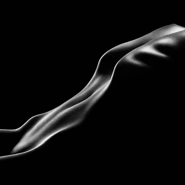 he image is a black and white photograph of a female nude. the body is positioned in a curve, with the back and buttocks prominently featured. the lighting is dramatic, creating strong contrasts between light and shadow, highlighting the curves and contours of the body. the overall effect is an abstract and sensual representation of the female form.  the image is minimalist in its composition, focusing solely on the body's shape and texture.