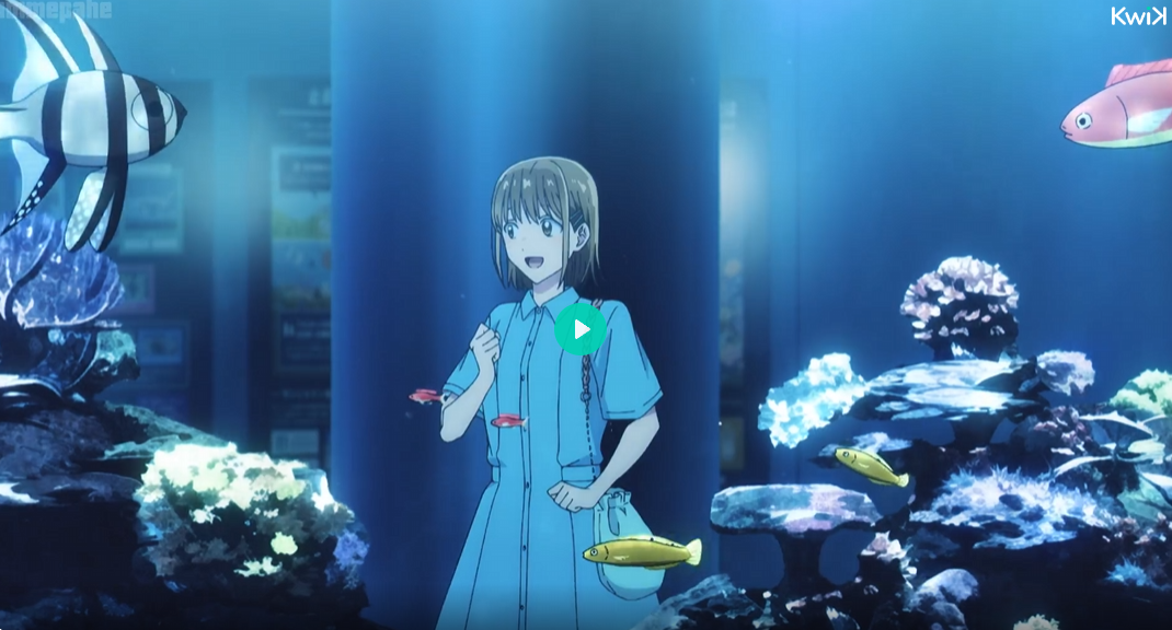 he image is a still from an anime featuring a young girl standing in front of a large aquarium.  she's smiling and appears happy. the aquarium is filled with various colorful fish, including a prominent banded angelfish in the foreground, and coral reef structures.  the overall atmosphere is serene and peaceful.  the style is characteristic of modern anime animation. the girl is wearing a light blue dress and carries a small bag. a play button is superimposed in the center.