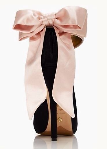 a pair of black suede stiletto heels with a large pink satin bow at the top. the heel is about 4 inches tall and the bow is very full and fluffy. the shoes are made by kate spade.