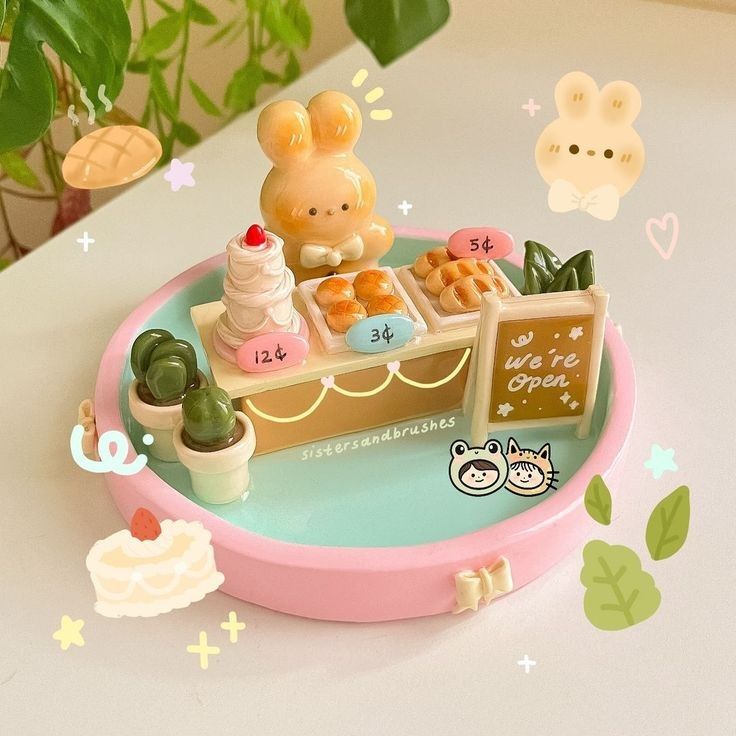 the image shows a miniature bakery display on a pink and turquoise circular base. the display features a bunny figure, cakes, bread, cacti in pots, and a sign that reads "we're open." price tags are displayed next to the baked goods. surrounding the display are various cartoon stickers and decorative elements.