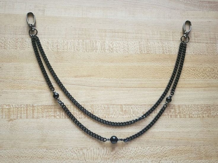 a closeup shot of a twostrand black wallet chain. each strand is interspersed with dark beads and terminates in a clasp. the chain is placed on a lightcolored wood surface.