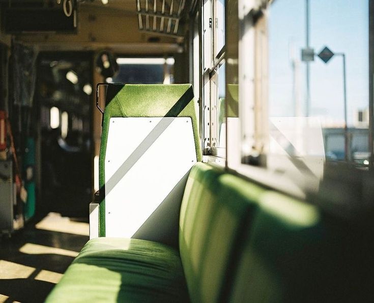 the image showcases a closeup view of a green upholstered seat inside a train or bus. sunlight streams through the window, casting shadows across the seat and the interior of the vehicle. the overall atmosphere is peaceful and serene. the focus is primarily on the seat and the play of light and shadow, while the background is slightly blurred but reveals the interior of the public transportation vehicle. the image evokes a sense of quiet contemplation and journey.