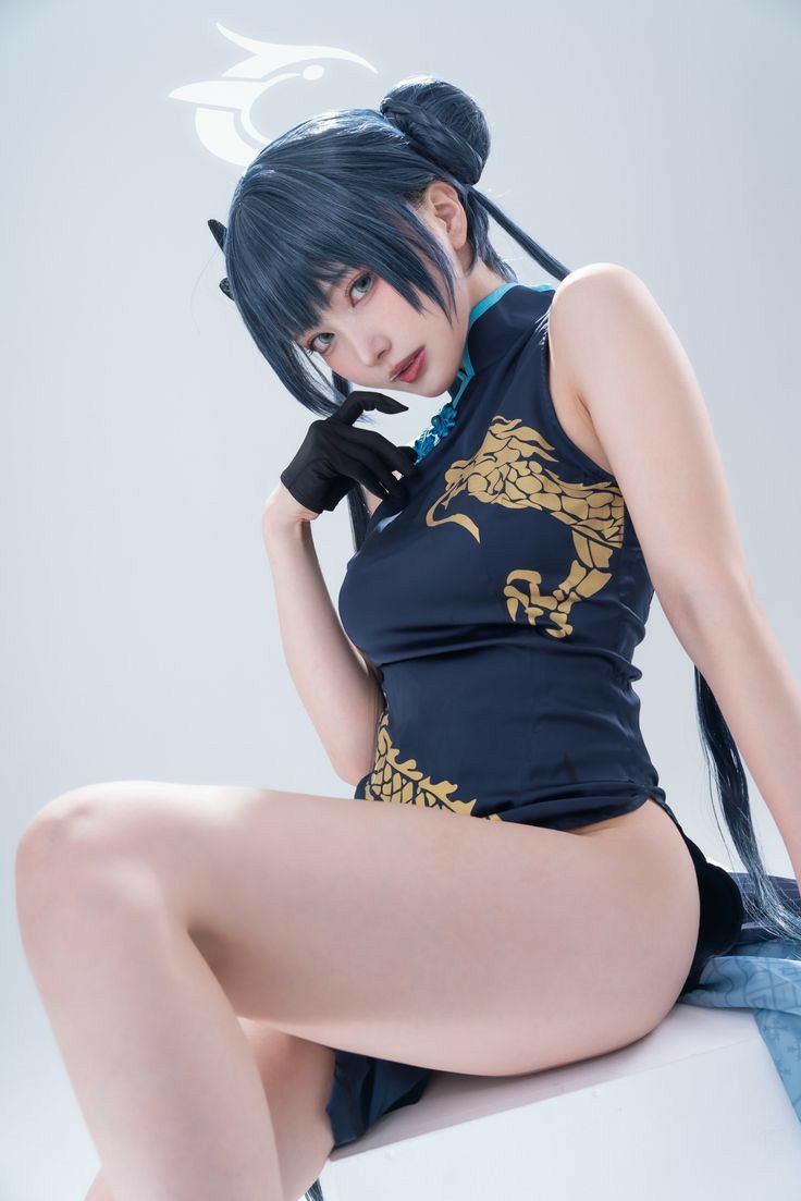 a young asian woman is posing in a studio. she is wearing a black cheongsam with gold dragon details, and her hair is styled in a bun. she is sitting with one leg crossed over the other, showcasing her long legs and thighs. her makeup is impeccable, and her expression is alluring. the overall feel of the image is elegant and glamorous. the background is a plain, light gray, ensuring the focus remains on the model. the image is welllit, highlighting the details of the costume and the model's features.