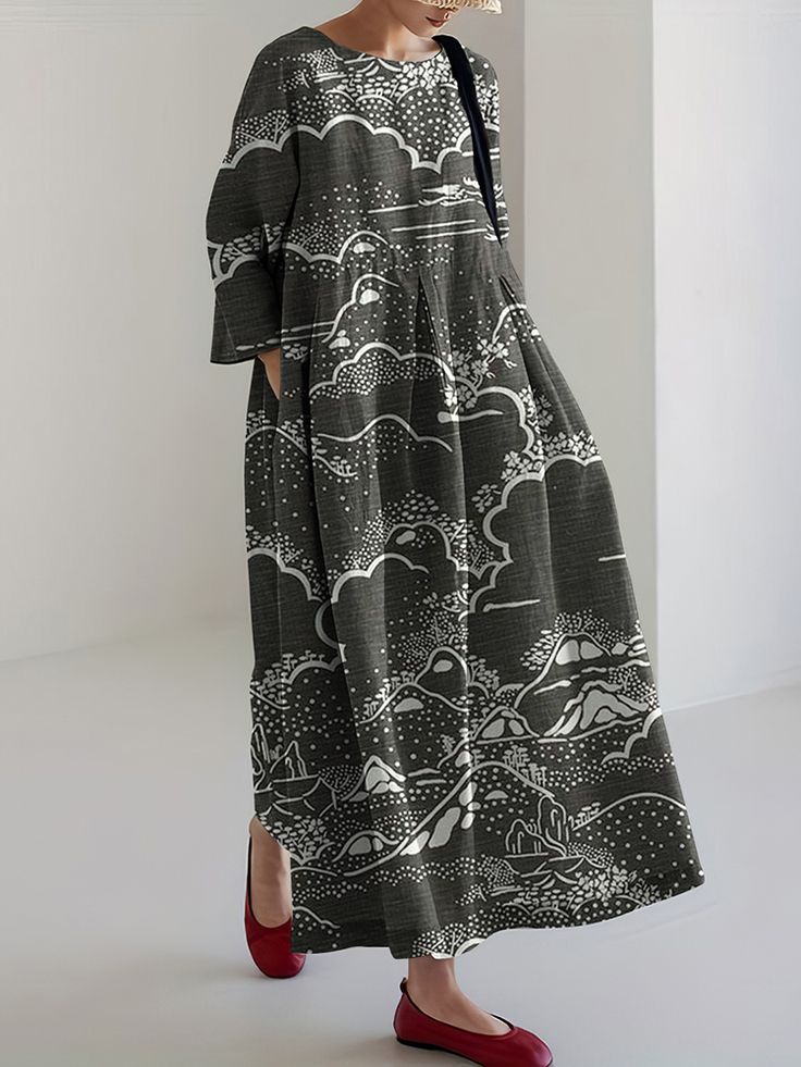 a woman is standing in a gray maxi dress with white landscape print. the dress is longsleeved, has a loose fit and a flowy style. she is wearing red flats and a straw hat.