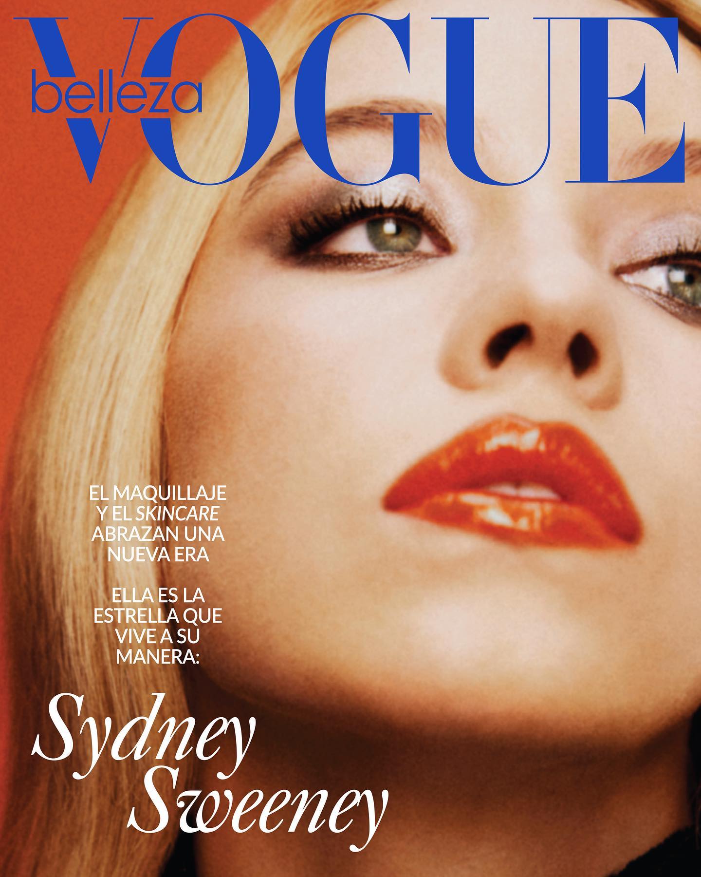 a magazine cover featuring a closeup portrait of actress sydney sweeney. the title "vogue" is prominently displayed in blue letters at the top. other text on the cover is in spanish and includes lines about makeup and skincare, and sweeney being a star who lives her way. sweeney has blonde hair, glossy lips, and dramatic eye makeup. the background is a solid orange color.