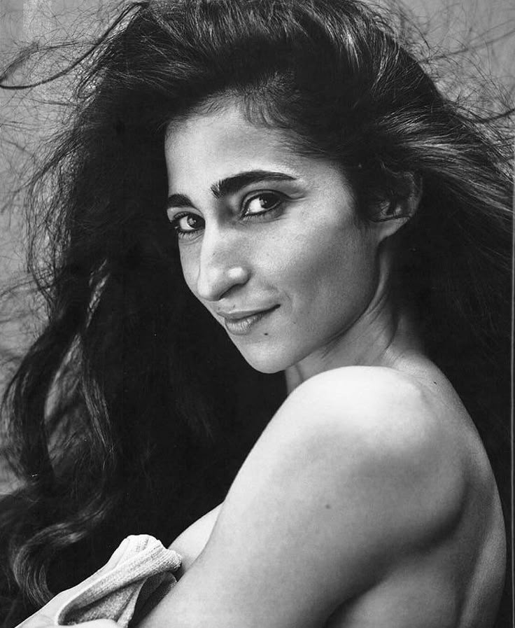 a black and white portrait of a woman with long, flowing hair. she is looking over her shoulder with a slight smile. her bare shoulder is visible in the foreground.
