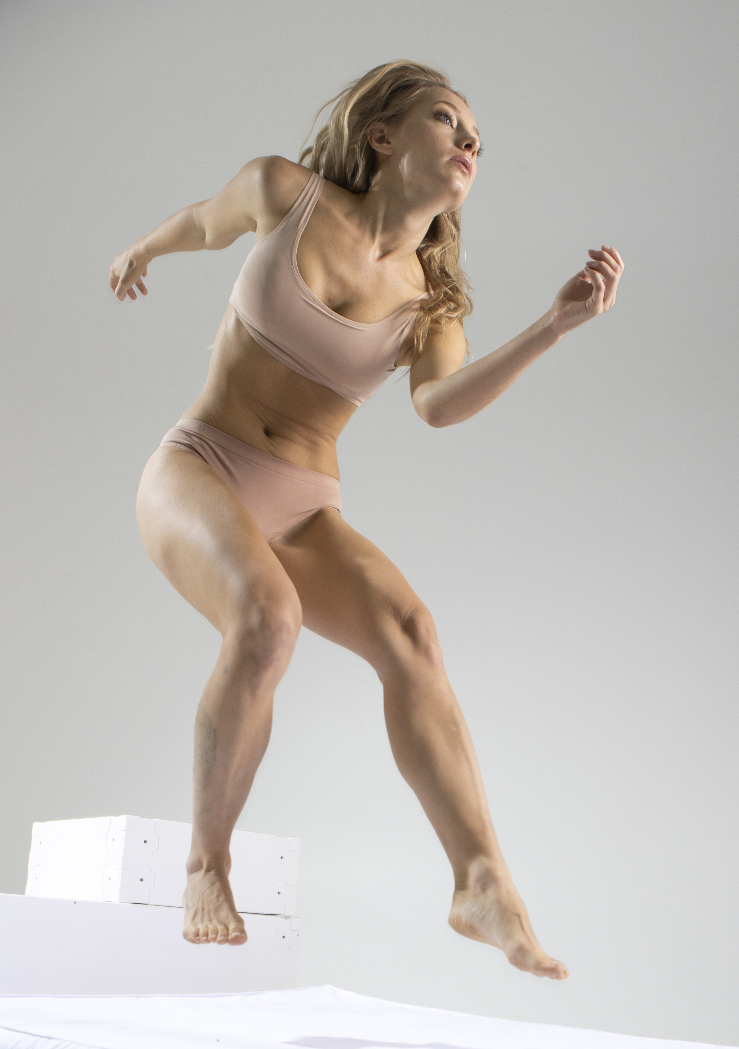a full shot of a muscular woman in a sports bra and underwear jumping in a studio. she is athletic and barefoot, captured in a dynamic, fitnessoriented pose.
