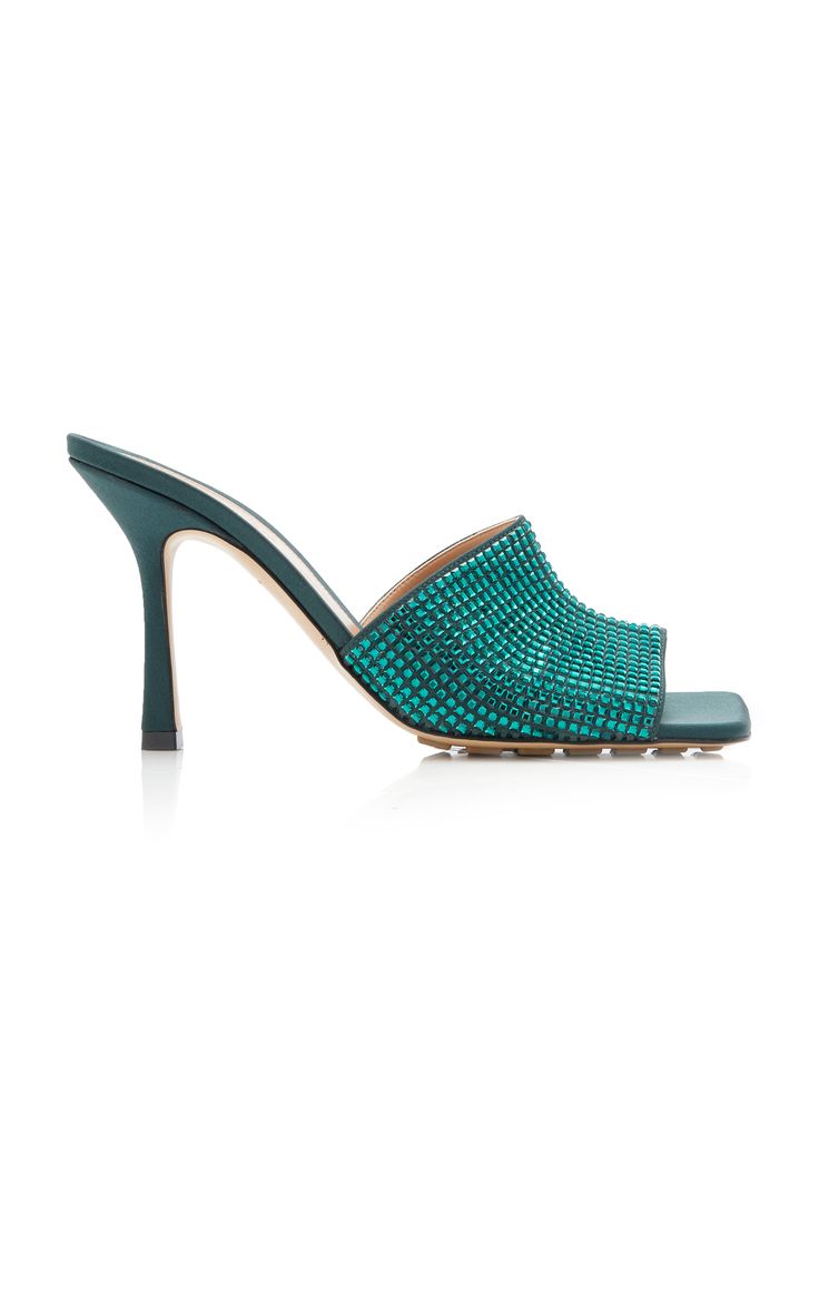 pair of teal green women's mules with a square toe and a high stiletto heel.  the shoes are embellished with crystals on the front.  the shoes are shown on a white background. the image is a studio shot, showing the shoes from a threequarter angle.