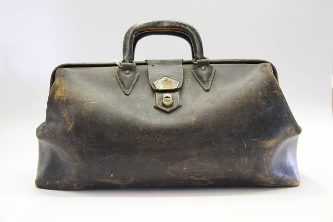 a worn leather doctor's bag sits against a white background. the bag is brown with a darker handle. it has a metal clasp.