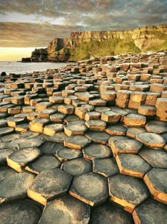 a panoramic shot of the giant's causeway in northern ireland. the image showcases the iconic basalt columns, which are a natural wonder and a popular tourist attraction. the columns are formed by volcanic activity and are arranged in a hexagonal pattern, resembling a giant's pathway. the photo captures the beauty of the coastal landscape, with the ocean in the background, a dramatic sky, and the rugged cliffs in the distance. the sun is setting, casting a golden glow over the scene.