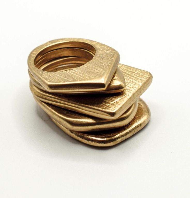 this image features a stack of four gold rings, each with a unique shape. the rings are made of brass and have a textured finish. the stack is arranged with the largest ring at the bottom and the smallest ring at the top. the rings are all in focus and the background is blurred. this image showcases the beauty and craftsmanship of handcrafted jewelry.