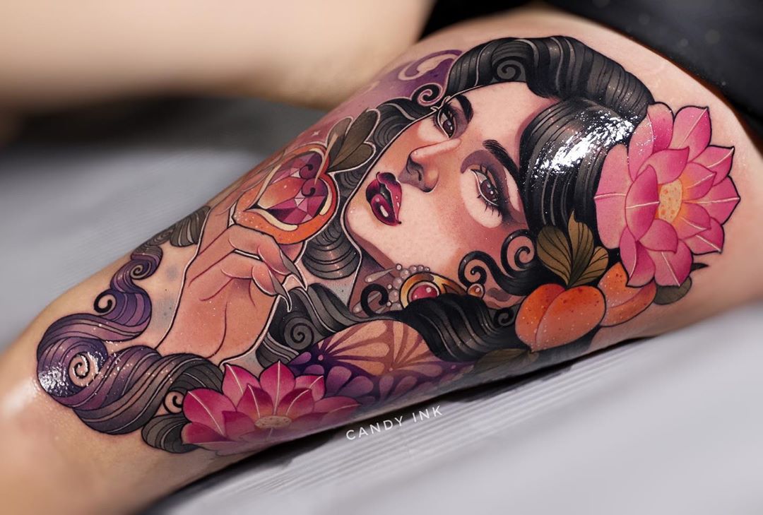 the image showcases a neotraditional tattoo of a woman on someone's thigh. the woman has dark, flowing hair adorned with jewels. she holds a stylized, heartshaped fruit, possibly a peach, with a glowing center. surrounding her are large, pink flowers, also likely peach blossoms. the tattoo has a vibrant color palette and smooth shading, characteristic of the neotraditional style.