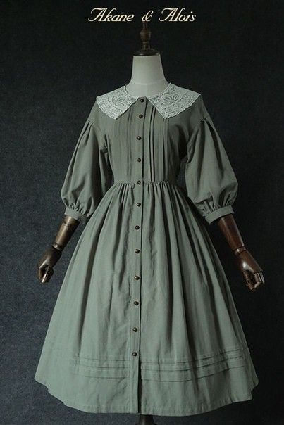 a vintage style green dress with lace collar displayed on a mannequin. the dress features long puff sleeves and a buttonup front. the background is a dark gray color.