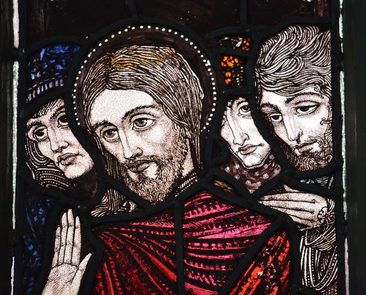 the image shows a stained glass depiction of jesus with a halo, surrounded by three other people. he is wearing a red robe. the art is religious, likely christian, representing a biblical scene or figures.